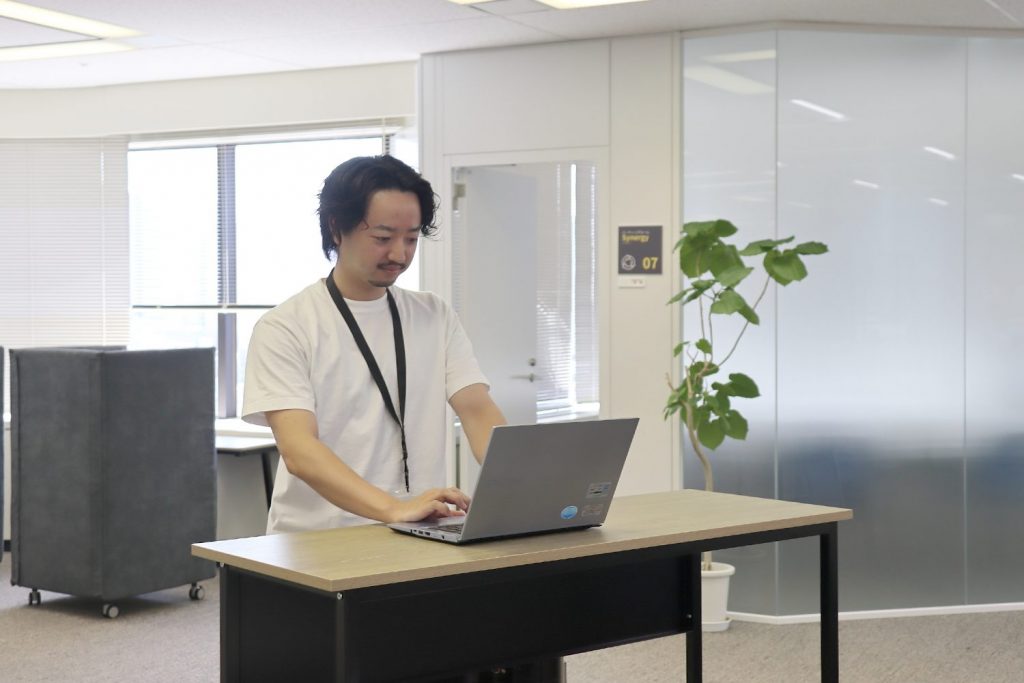 立ってパソコン作業をするHさん。