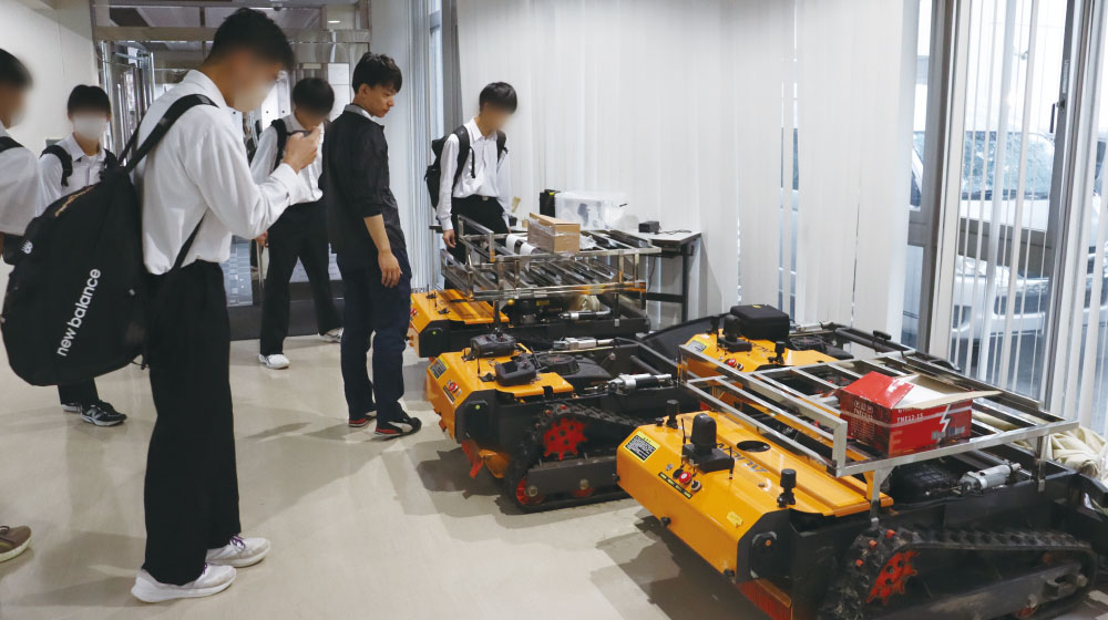 雄城台高校の生徒がciRobotics賀来事業所で自動リモコン草刈り機GA45Xを見学している様子